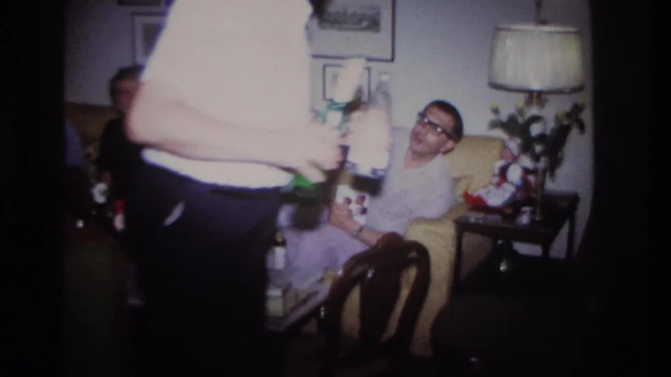 A close foreground figure partly blocks a Rockaway Beach living-room party scene as guests sit with drinks behind him.