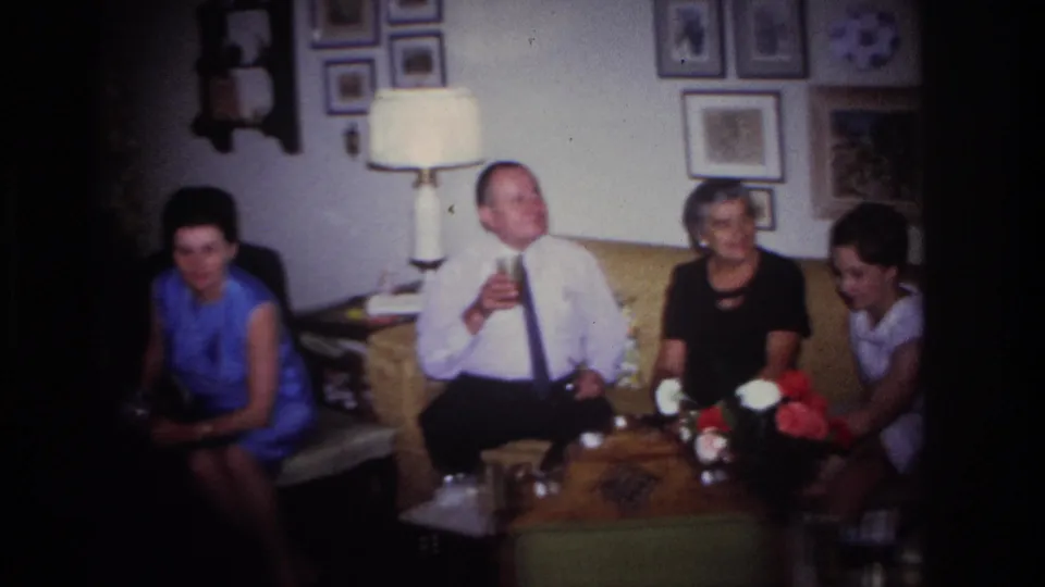 1967 Rockaway Beach frame of adults seated in a private living room with drinks, flowers, lamps, and framed pictures.