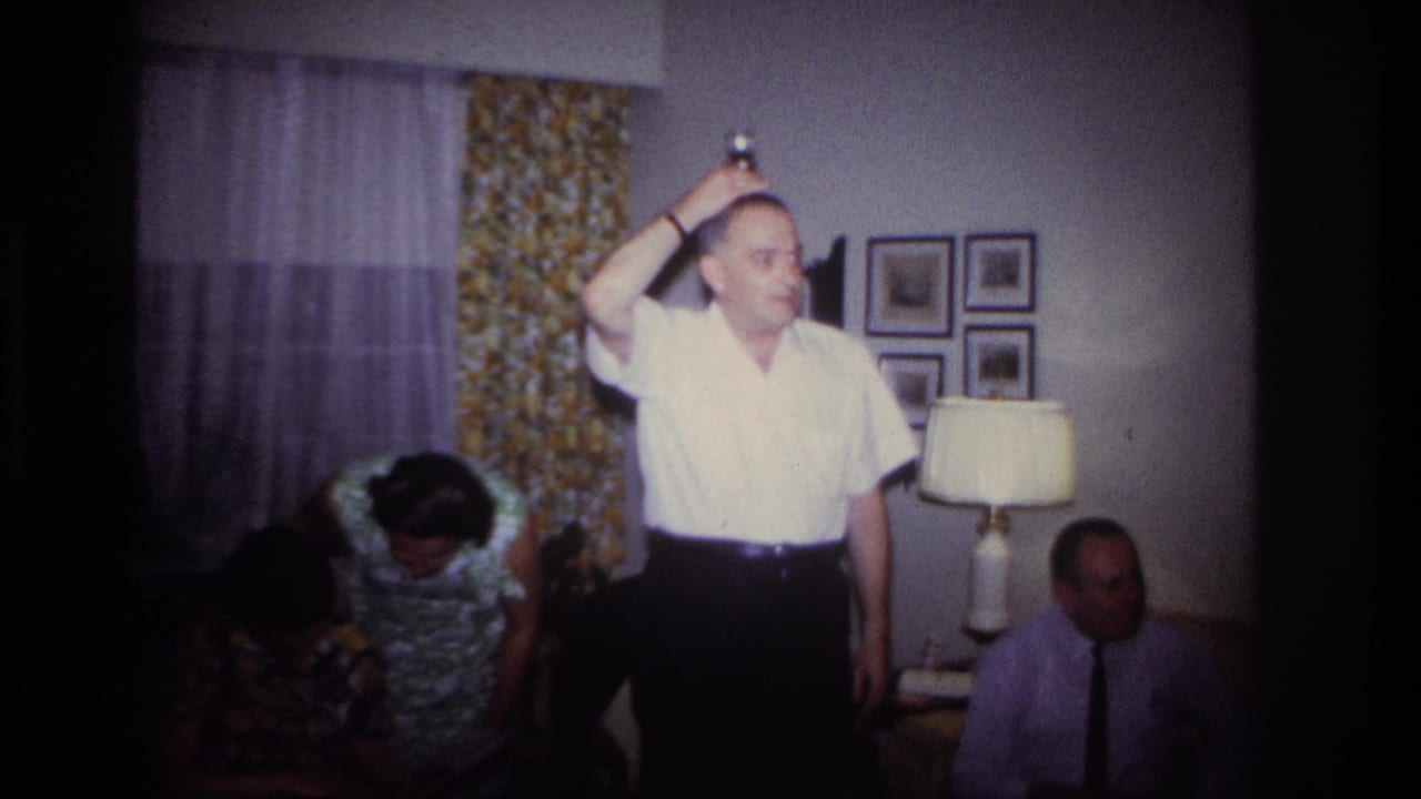 Man in a white shirt stands with one arm raised as guests remain seated nearby.