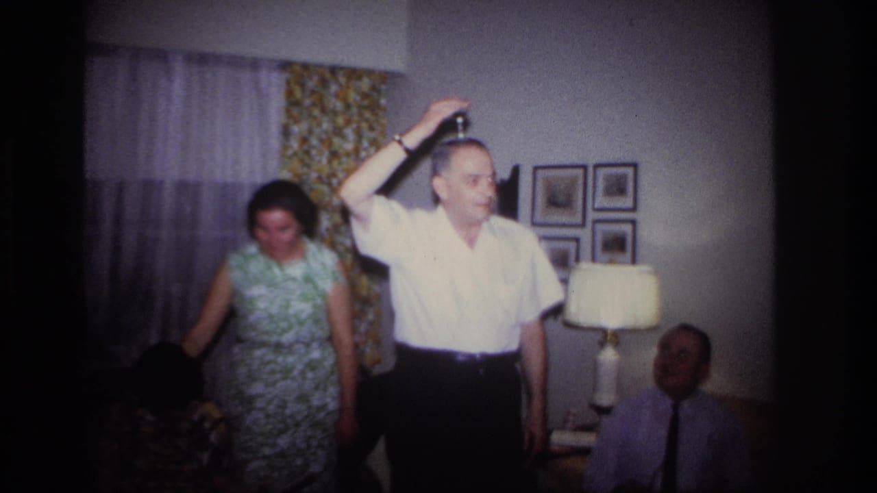 Man balances or places a small object on his head as a woman stands behind him.