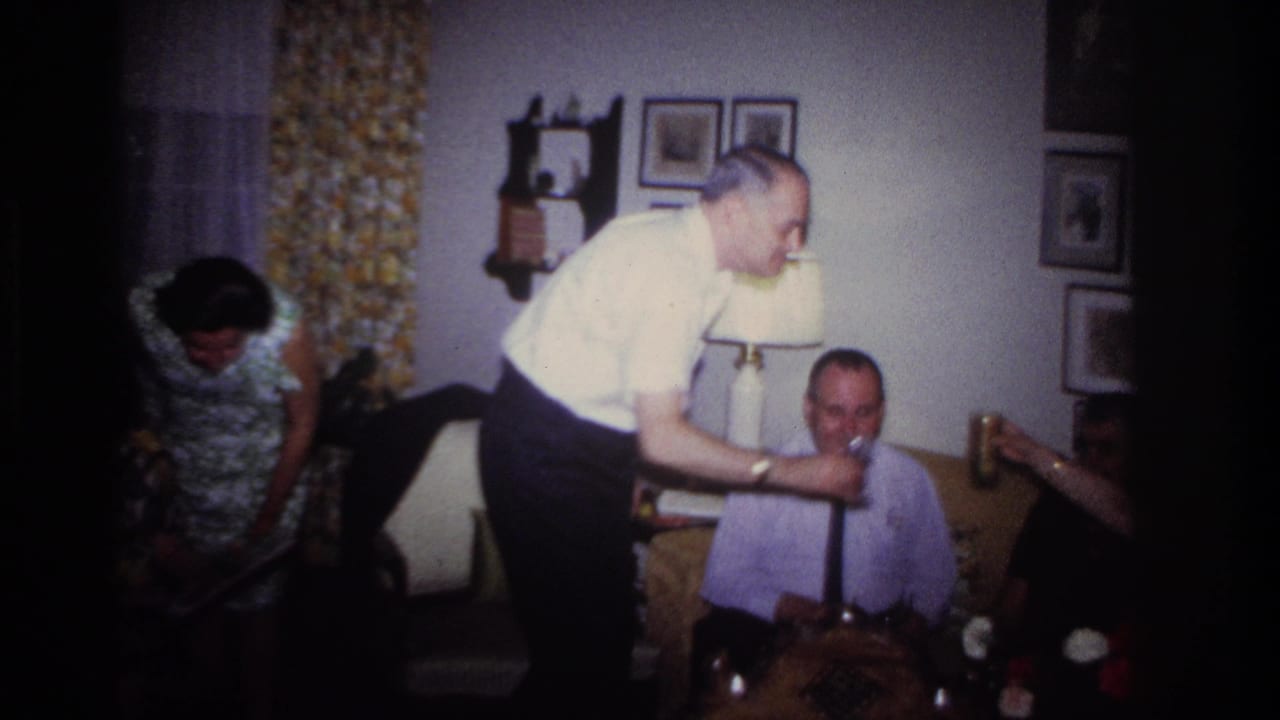 Rockaway Beach 1967 home-movie frame showing adults in a living room during a toast, with framed pictures and patterned curtains behind them.