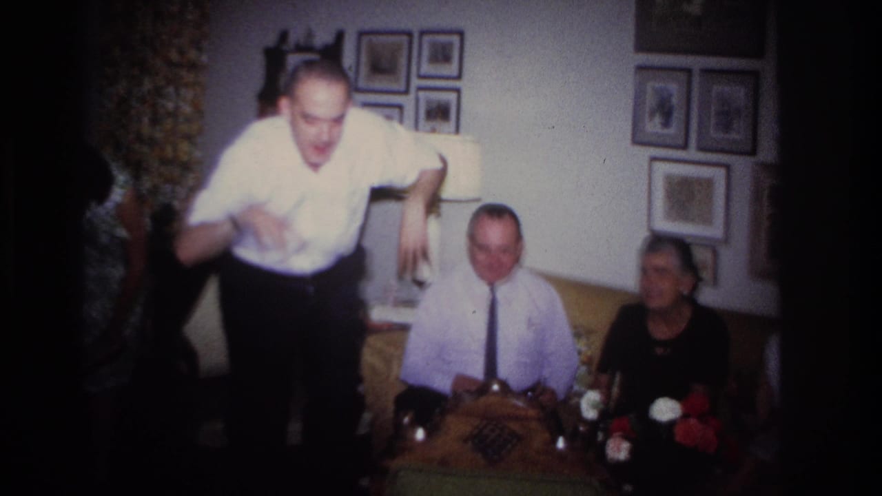 Man in a white shirt dances near two seated adults in a living room.