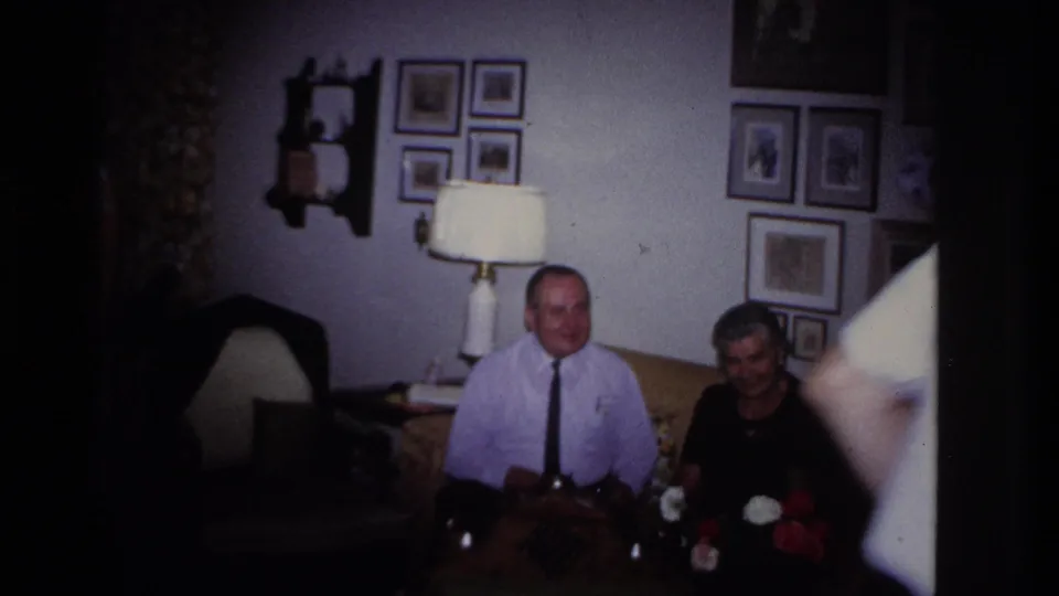 Two seated adults smile from the couch while the dancing man exits the right edge of the 1967 living-room frame.