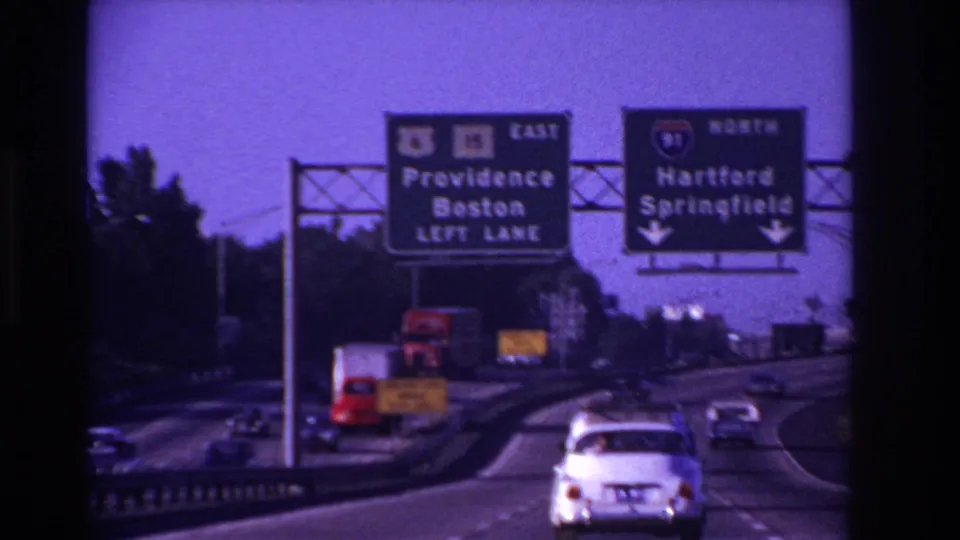 Passenger-view highway footage shows 1960s cars approaching overhead signs for Providence, Boston, Hartford, and Springfield.