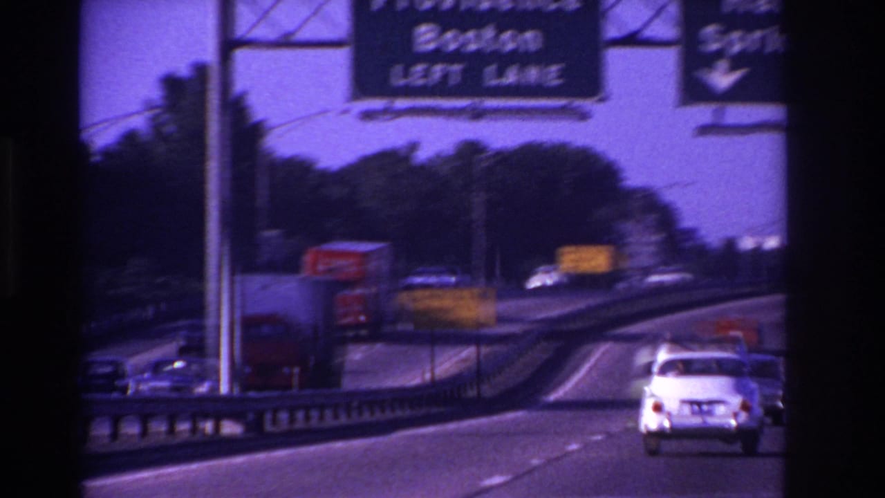 Highway view from a moving car with overhead signs, traffic, and a white sedan ahead.