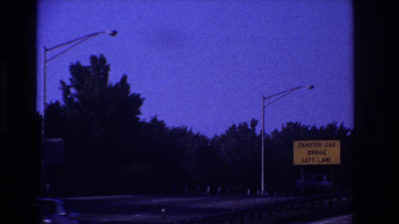 Roadside sign for Charter Oak Bridge left lane beside trees, streetlights, and guardrail.