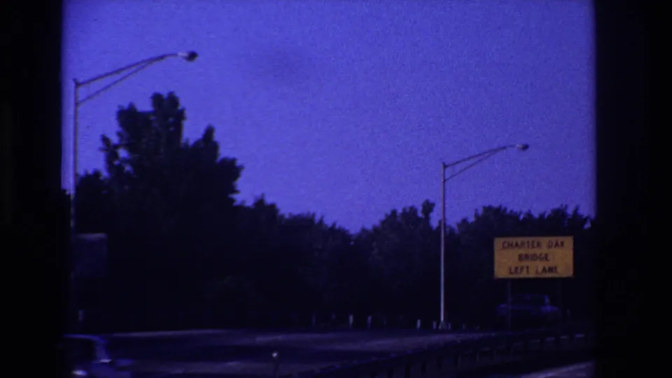 Highway POV frame showing a Charter Oak Bridge left-lane sign, dark roadside trees, streetlights, and a guardrail in low light.