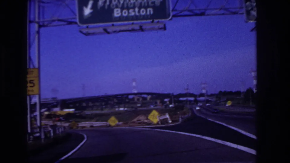 Forward-facing 8mm road view showing a highway curve, construction-style warning signs, and an overhead Providence and Boston sign.