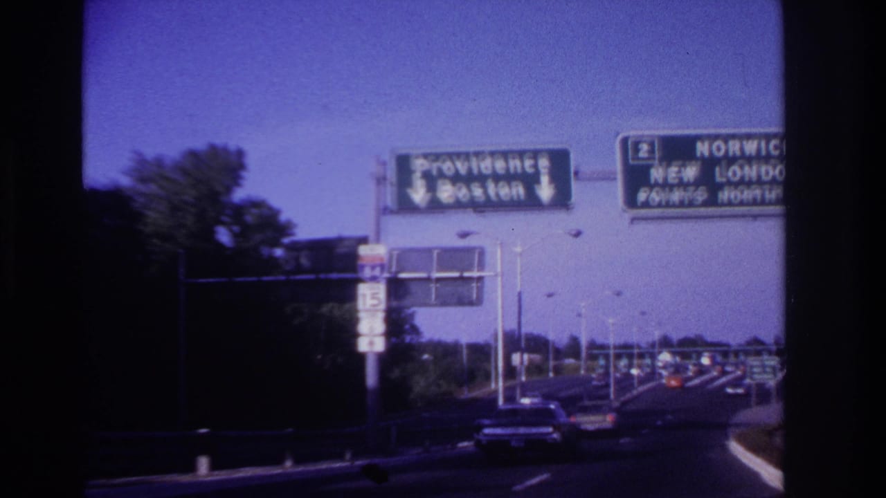 Highway traffic passes beneath large green signs for Providence and New London.