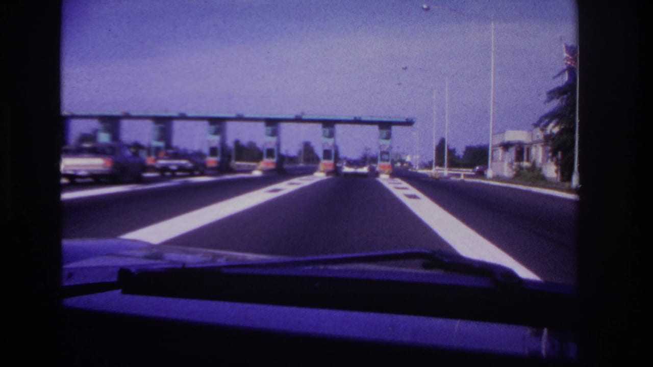 1967 Rockaway Beach highway view from inside a car, with white lane markings leading toward a toll plaza.