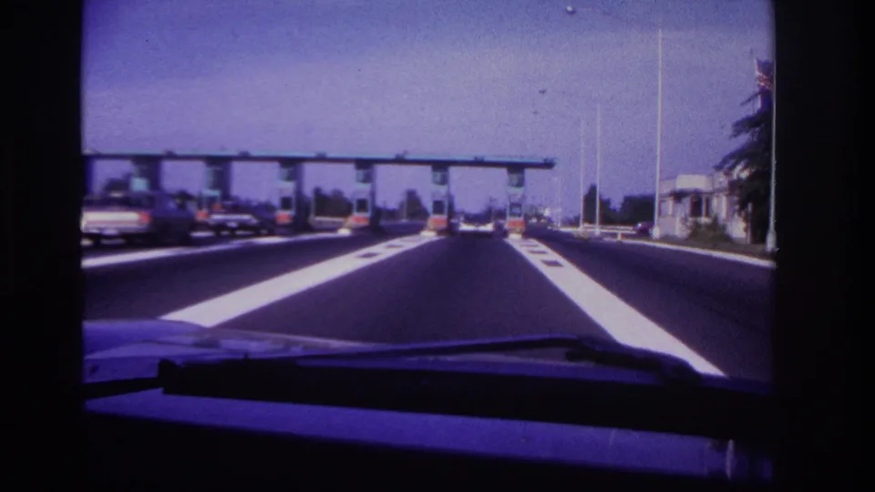 1967 Rockaway Beach highway view from inside a car, with white lane markings leading toward a toll plaza.