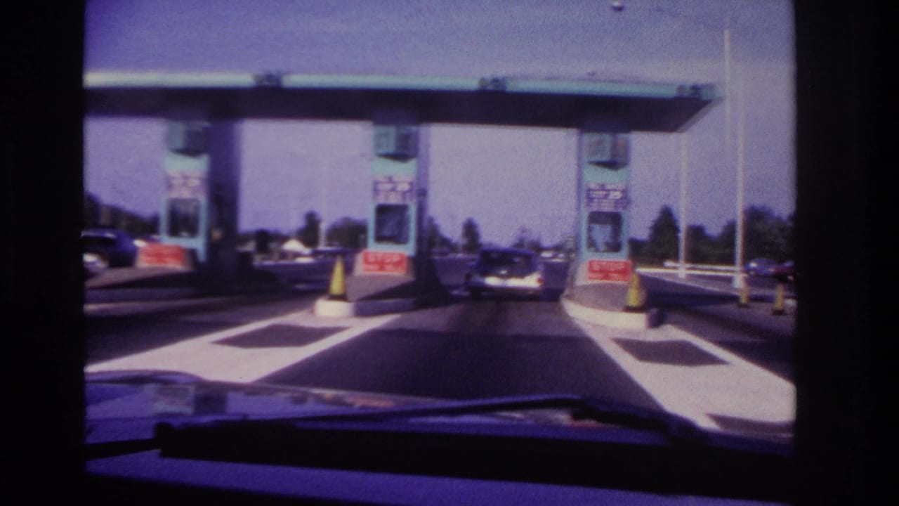 1967 Rockaway Beach-area driver's view approaching teal toll booths with red stop-pay-toll signs, yellow cones, and a car ahead.