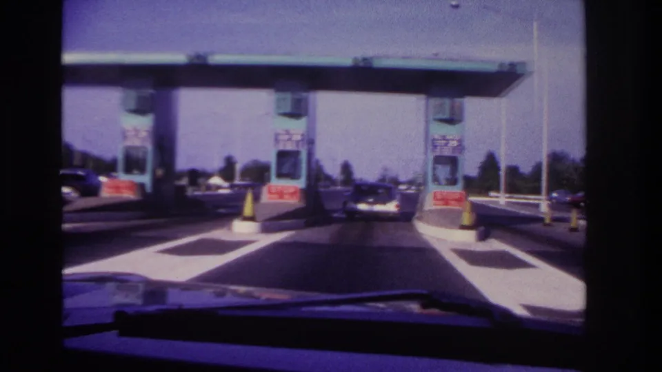 1967 Rockaway Beach-area driver's view approaching teal toll booths with red stop-pay-toll signs, yellow cones, and a car ahead.