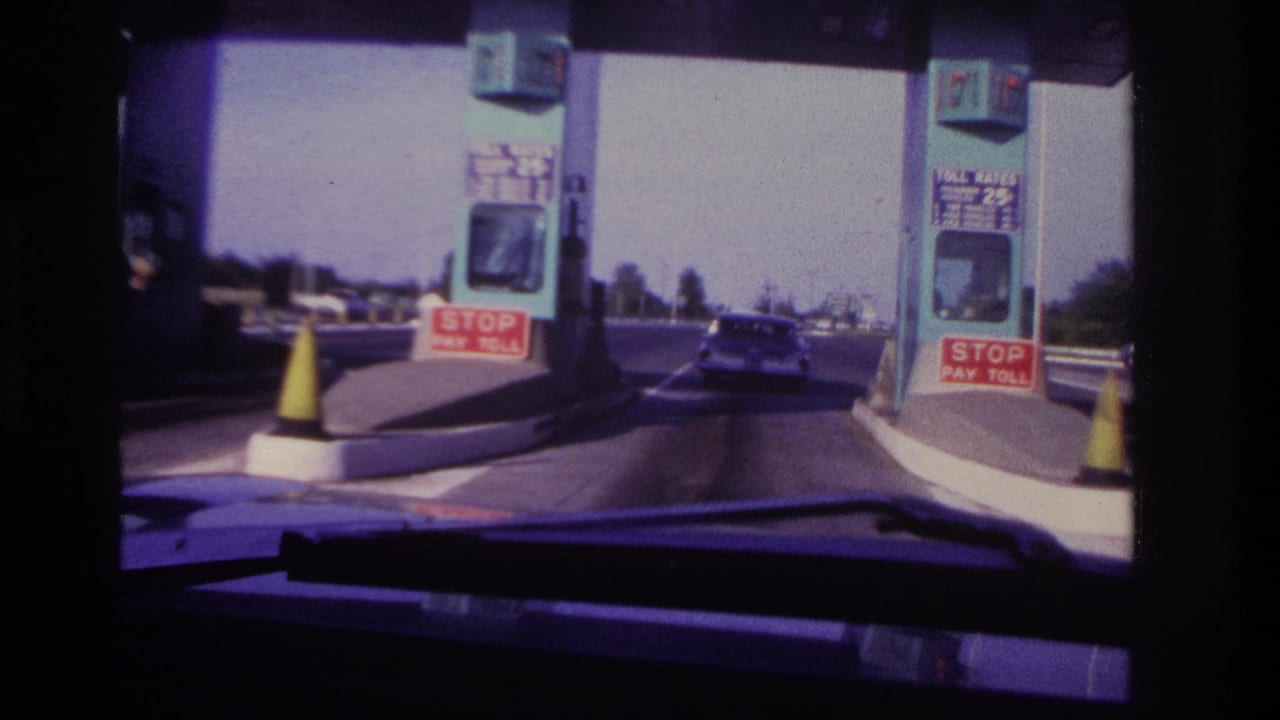 Car passes between toll booths with road lanes visible beyond the plaza.