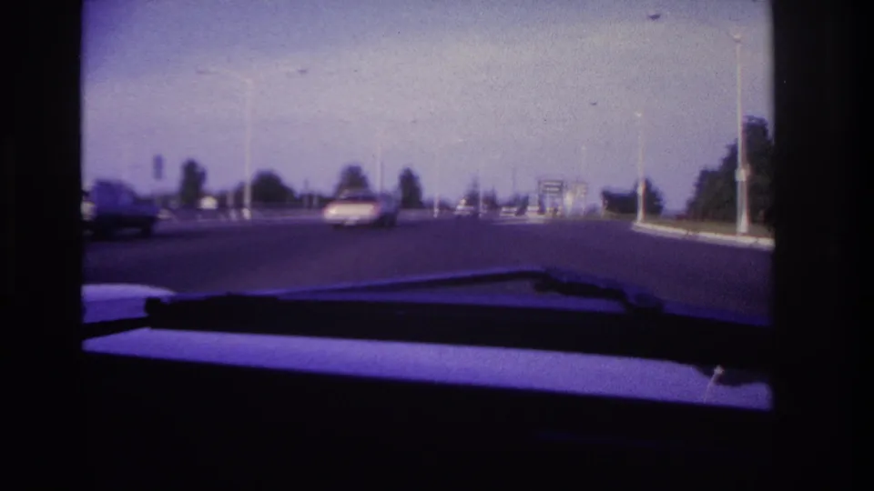 1967 home-movie frame from Rockaway Beach showing a road seen through a car windshield with traffic ahead.