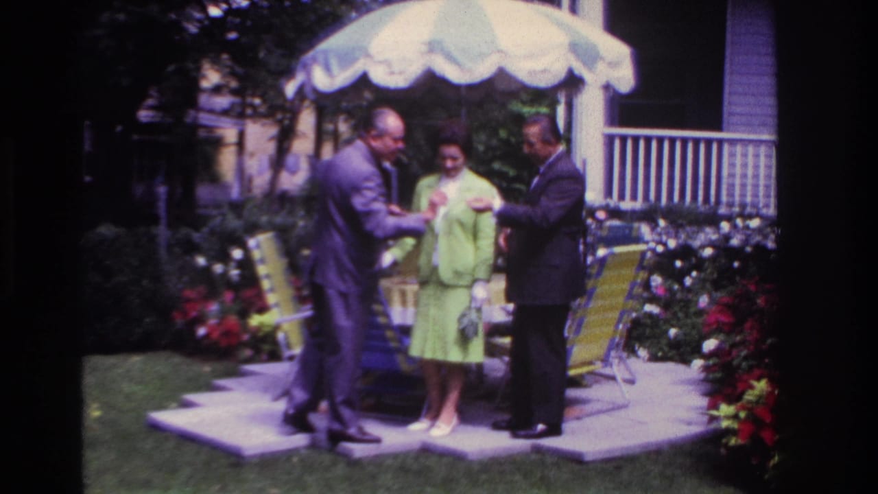 Two men and a woman stand beneath a patio umbrella, looking toward a small paper.