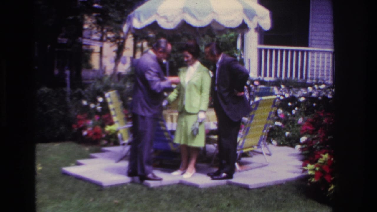 Three adults stand on a backyard patio while one man points to a pamphlet.