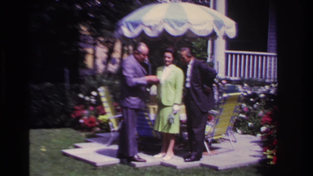 The adults remain grouped on the Rockaway Beach patio, with the woman holding a small bouquet and one man looking down at his hands.