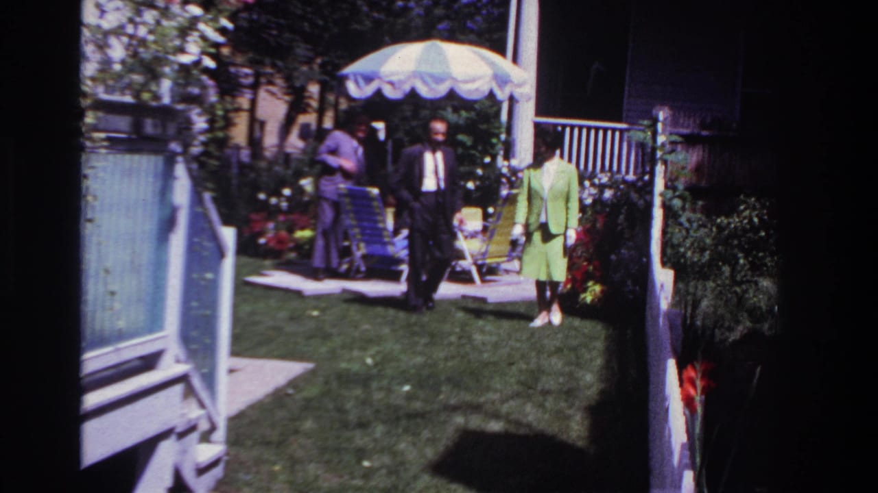 Man and woman walk across a backyard while another man stands by patio chairs.