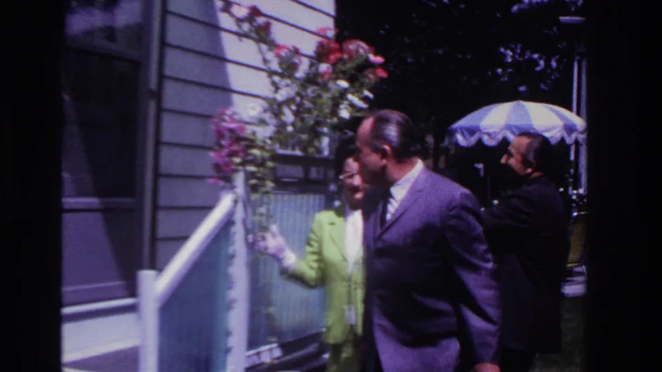 At the end of the Rockaway Beach porch moment, the men shift position near the woman, with flowers, siding, and the umbrella still visible.