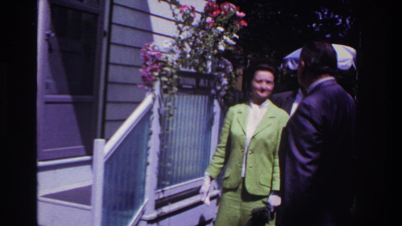Woman in lime green stands smiling on porch steps as two suited men face her.