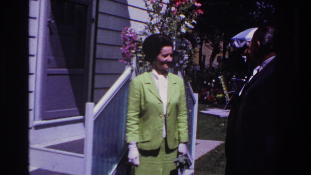 Woman in a lime green suit stands near porch steps while a man in a dark suit faces her.