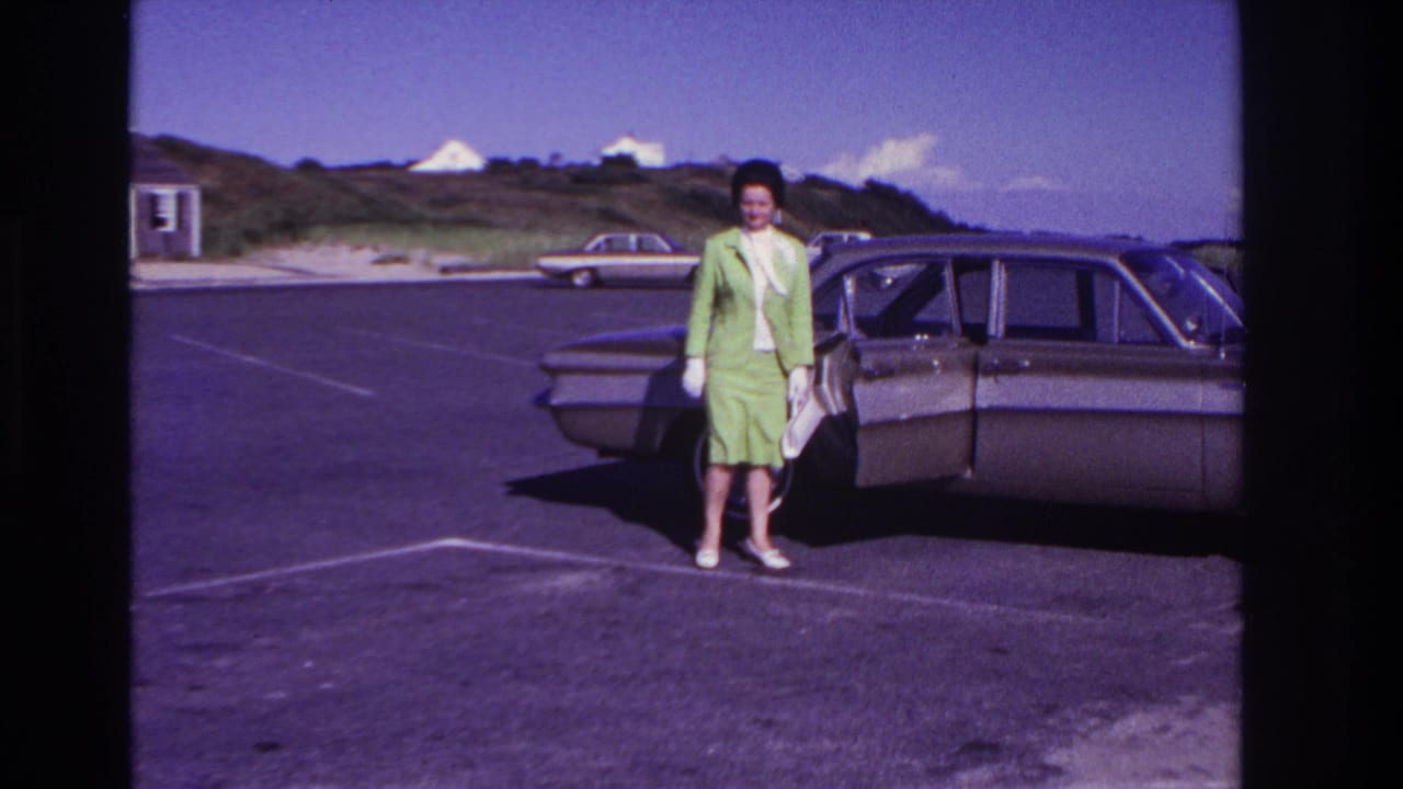 Woman faces the camera beside a sedan with the passenger door open.