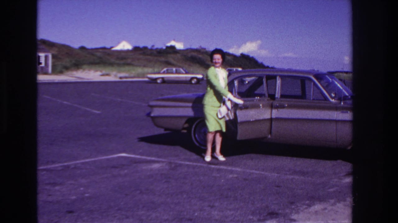 Woman smiles beside the sedan while holding a white purse in the parking lot.