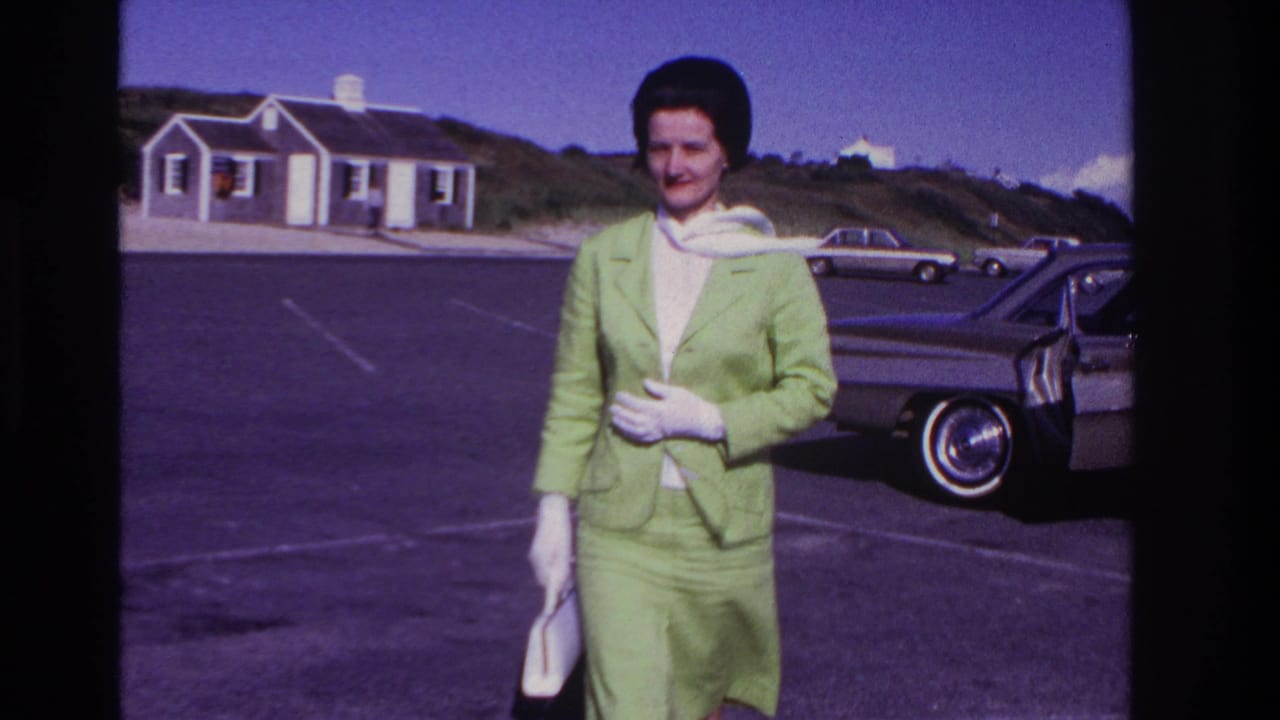 At Rockaway Beach in the stated 1967 footage, a woman in a green suit and white gloves stands near a parked mid-century car.