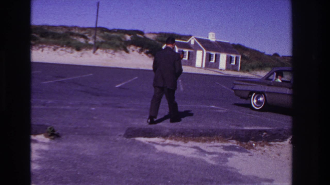Suited man walks farther across the parking lot toward a parked classic car.