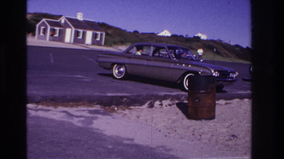 1967 Rockaway Beach frame with a classic sedan, a person near the front passenger area, and beach-lot surroundings.