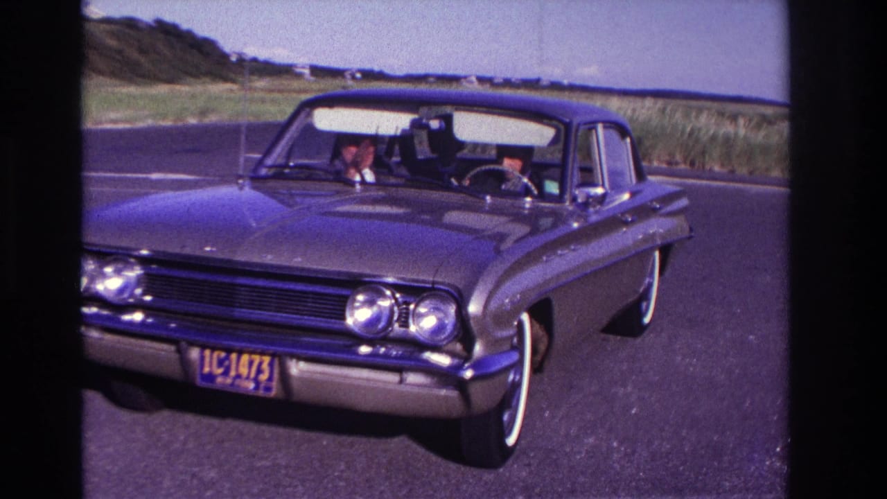 Classic sedan seen from the front on a road, with driver and passenger area visible through the windshield.