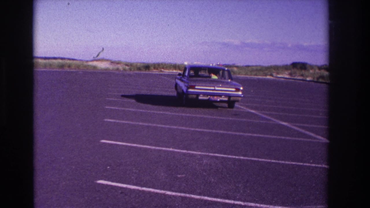 Sedan farther away in a broad parking lot with dunes on the horizon.