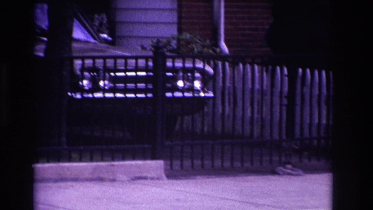 Car headlights seen behind a dark metal fence at night.