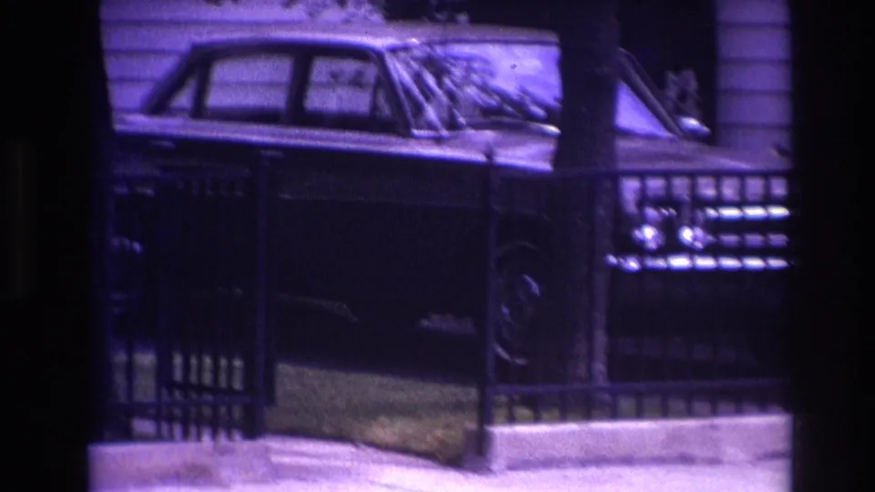The final frame shows the sedan's side and front behind a fence, with house siding and a porch area in low light.