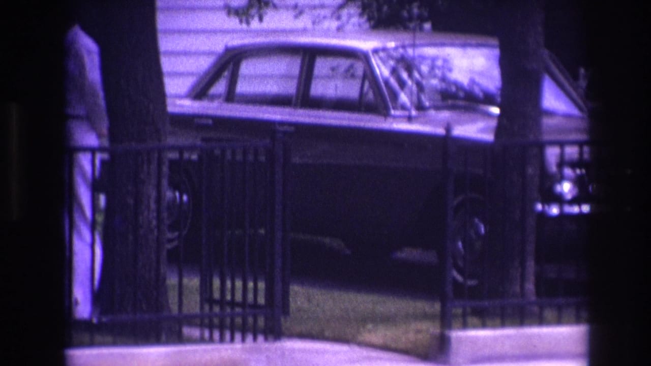 1967 Rockaway Beach home-movie frame showing a man in white clothing near a metal railing, trees, house siding, and a parked sedan.