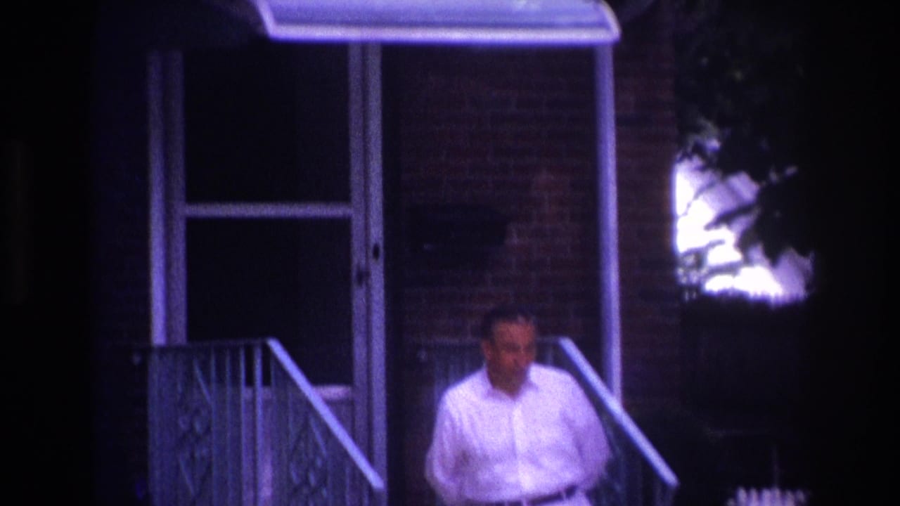 1967 Rockaway Beach frame with a man near porch steps, metal railing, brick facade, and dark doorway in a purple-tinted night scene.