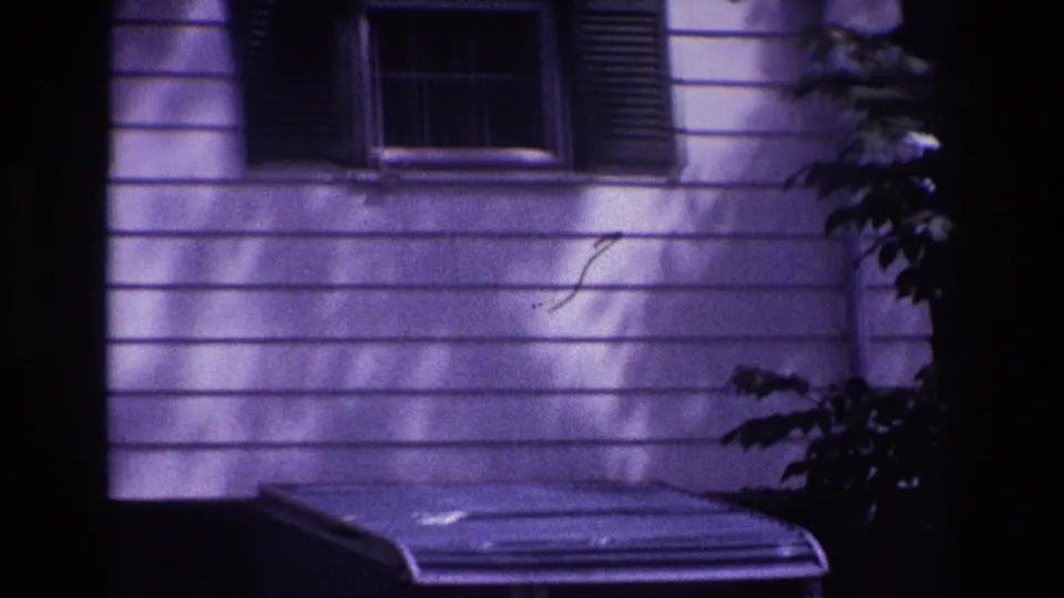 1967 Rockaway Beach home-movie frame focused on a residential facade with shuttered window, awning, siding, and tree shadows at night.