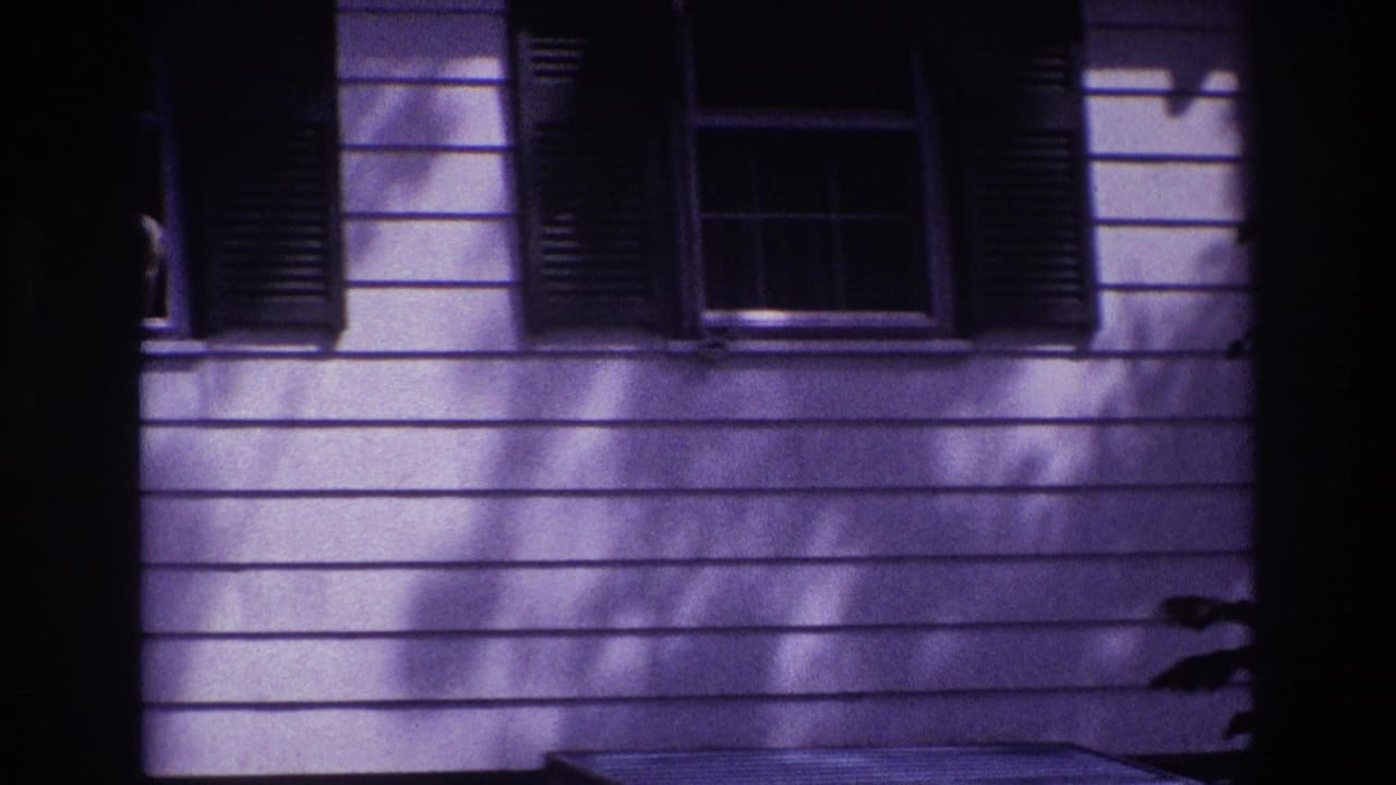 1967 Rockaway Beach home-movie frame showing a dim house facade with horizontal siding, dark shutters, and shadowed windows.