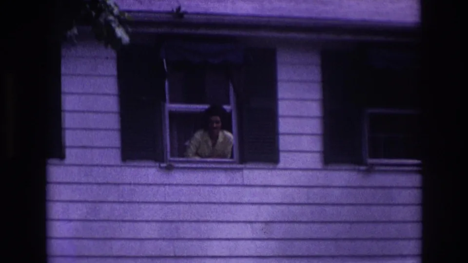 1967 home-movie still from Rockaway Beach showing a woman leaning from an open window of a residential house.