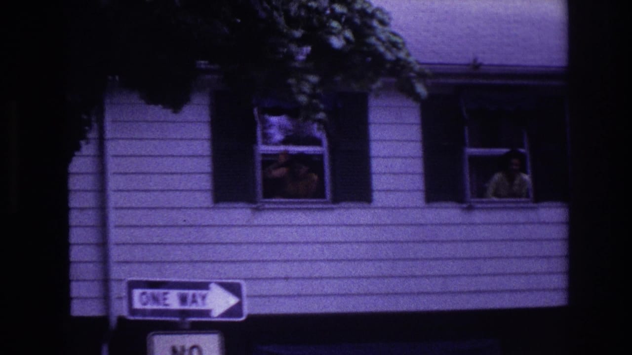 Upper story of a clapboard house with people at open windows and a One Way sign below.