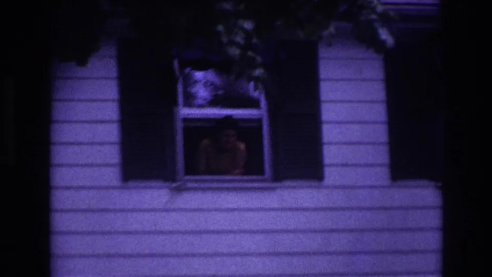 Closer 1967 Rockaway Beach home-movie view of a person leaning at an upper window with shutters and siding visible.