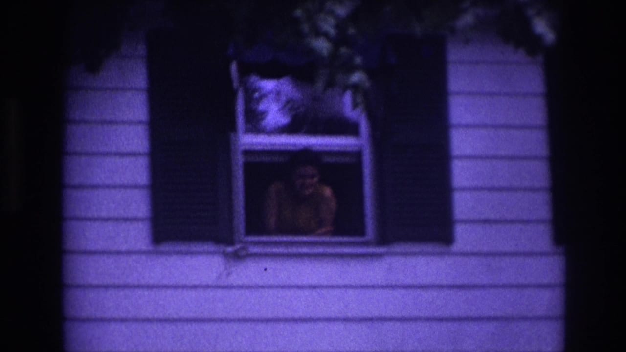 1967 Rockaway Beach home-movie frame showing a person at an upstairs window of a white-sided house with black shutters.