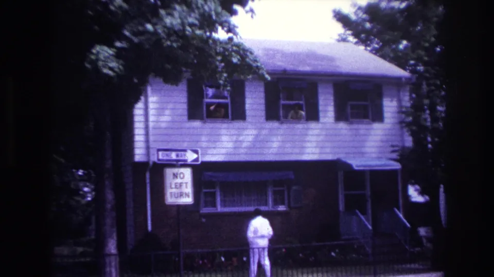 Rockaway Beach residential street frame with a man in white below upstairs windows and posted traffic signs.