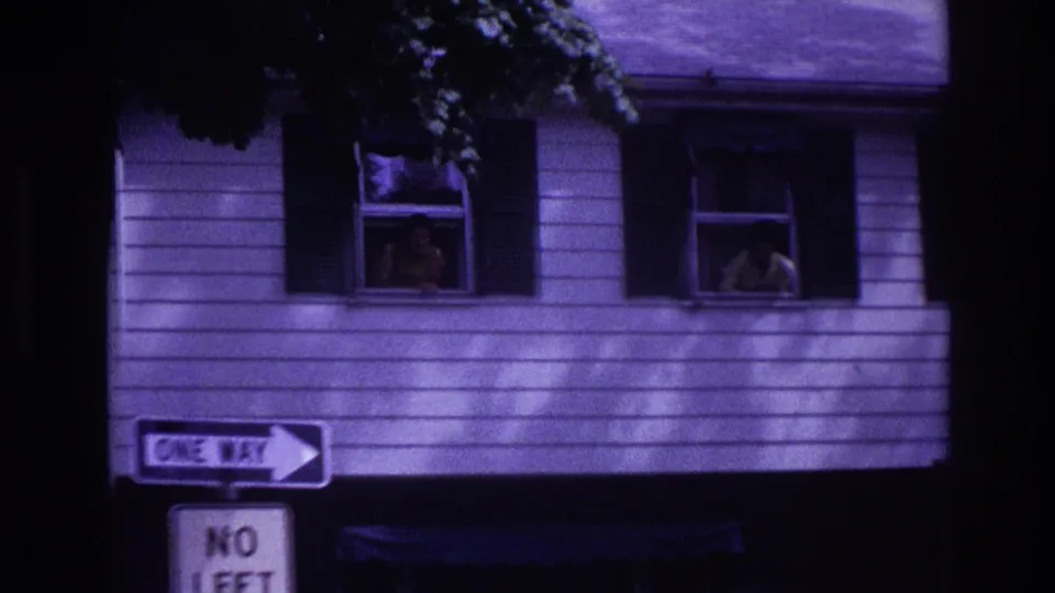Close 8mm frame of a Rockaway Beach house exterior with people visible in upper windows above traffic signs.