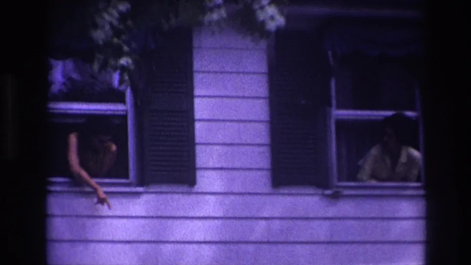 1967 Rockaway Beach frame with two adults at adjacent second-story windows, including one person extending an arm from the left opening.