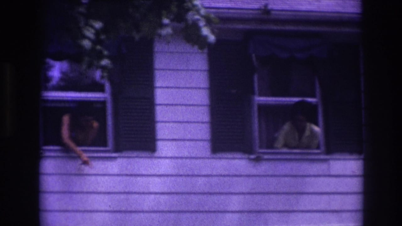 Rockaway Beach 1967 home-movie frame showing people at upstairs windows of a white-sided house with dark shutters.