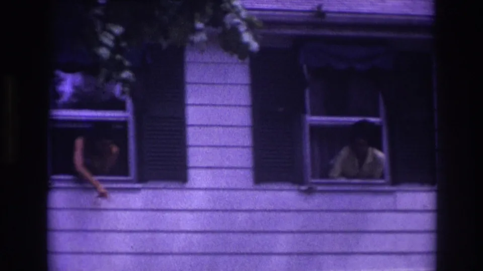 Rockaway Beach 1967 home-movie frame showing people at upstairs windows of a white-sided house with dark shutters.