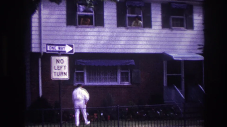Rockaway Beach 1967 street-level frame showing a man near a fence, traffic signs, awnings, and upstairs windows.