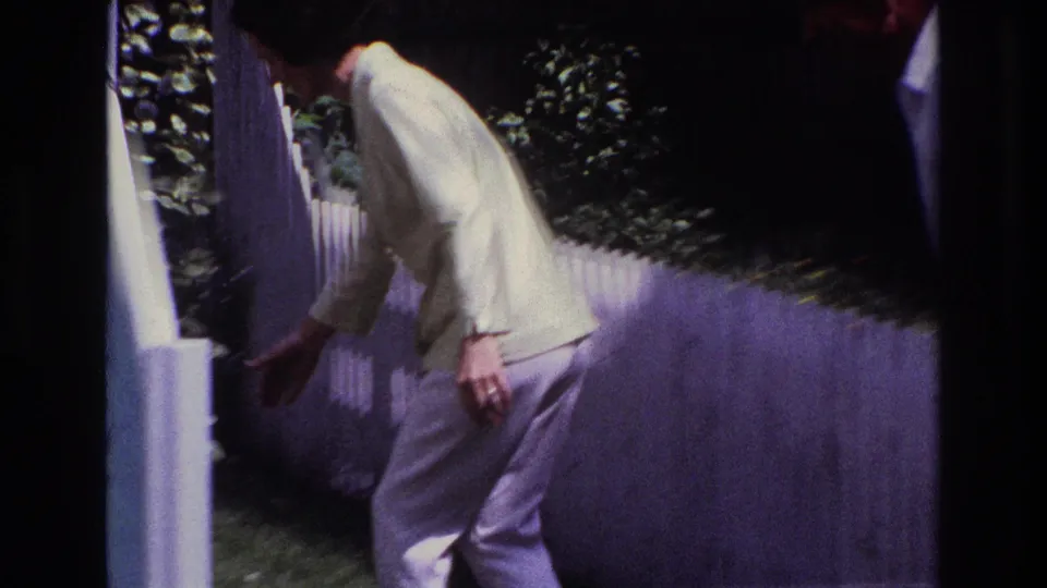 A woman in light clothing bends near the white fence and steps, with plants and lawn visible in the background.